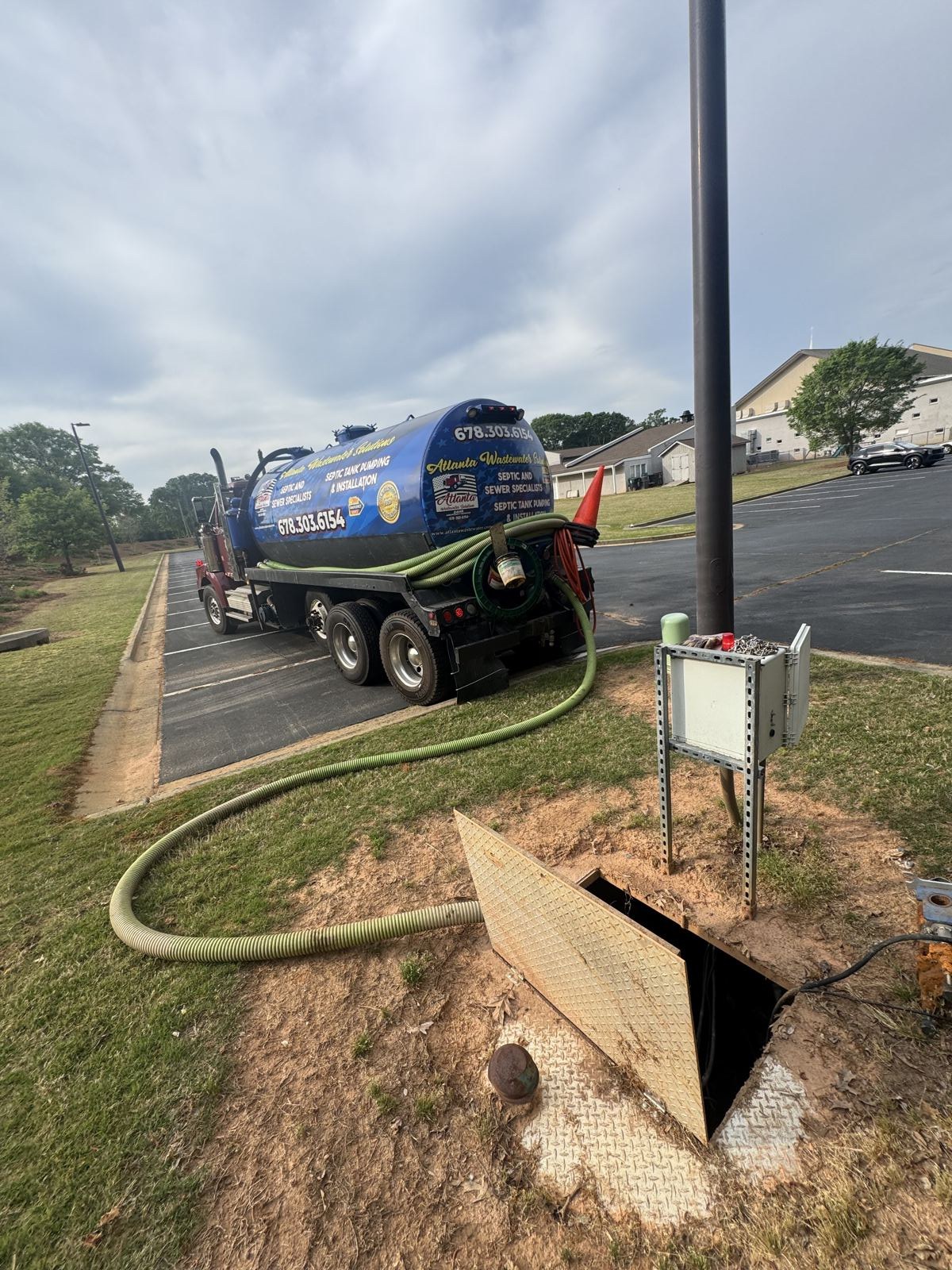 Septic service truck parked curbside with pump hose run to a residential tank