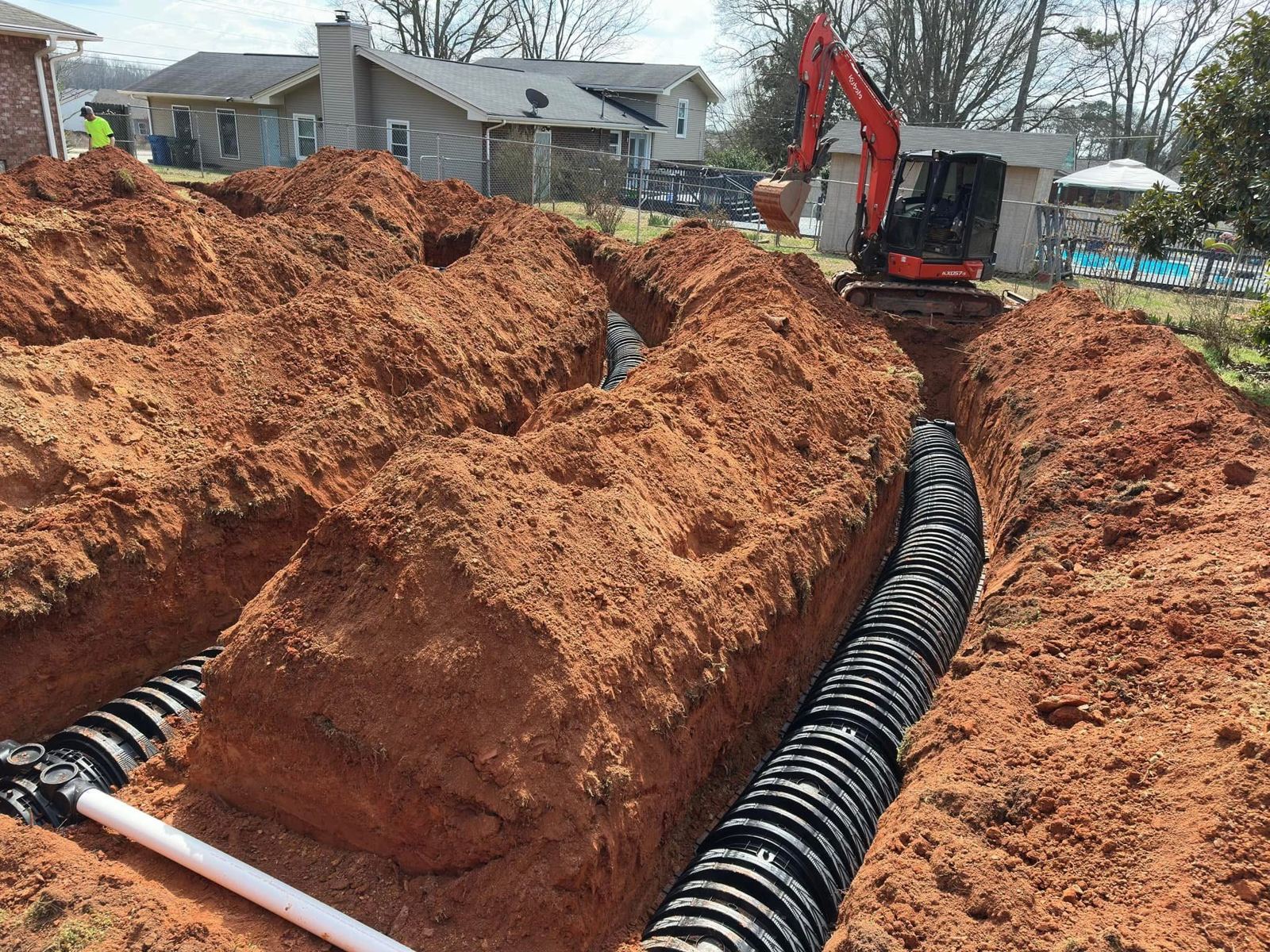 Excavator trenching a yard in red Georgia clay for a drainfield repair