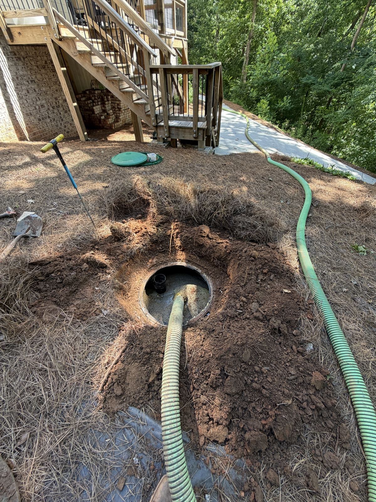 Green suction hose run into a residential septic tank access beside a home during a pump-out